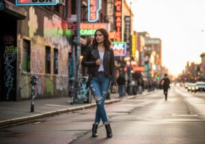 Młoda kobieta w czarnej skórzanej kurtce stoi na ulicy z graffiti i neonami podczas złotej godziny